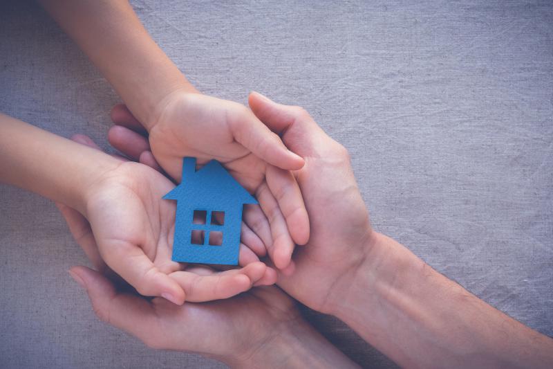 Two pairs of hands holding the blue cutout of a small house