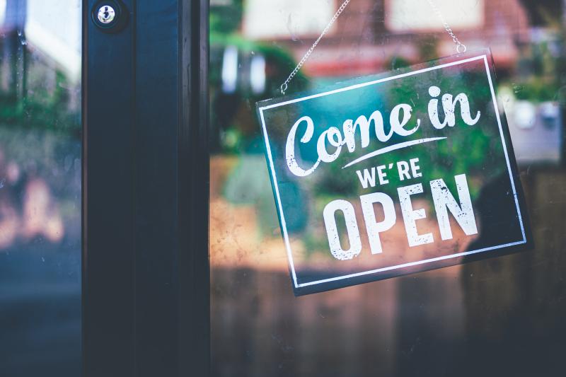 A green sign hangs on a glass door reading "Come in, we're open"